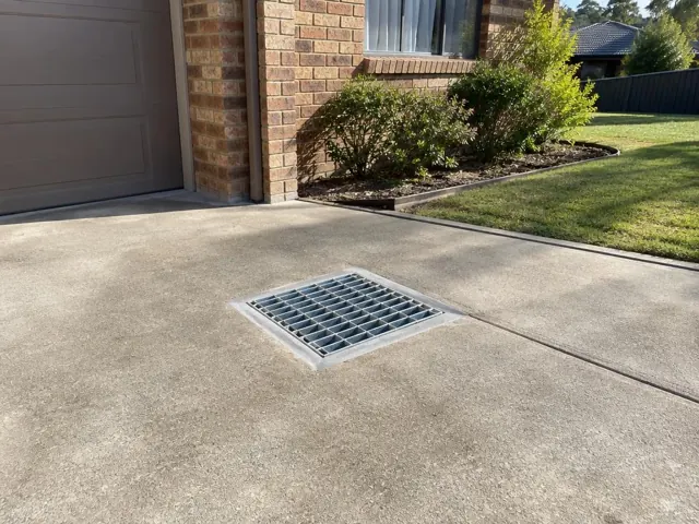 Clean outdoor driveway drain grate set in concrete beside a brick house in Baulkham Hills